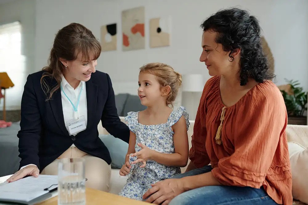 A behavioral health professional meets with a mother and young daughter in a warm, welcoming home setting