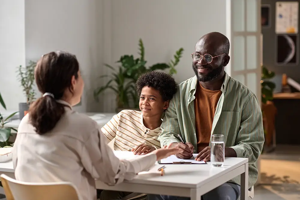 A child leaning against their dad while talking to a worker